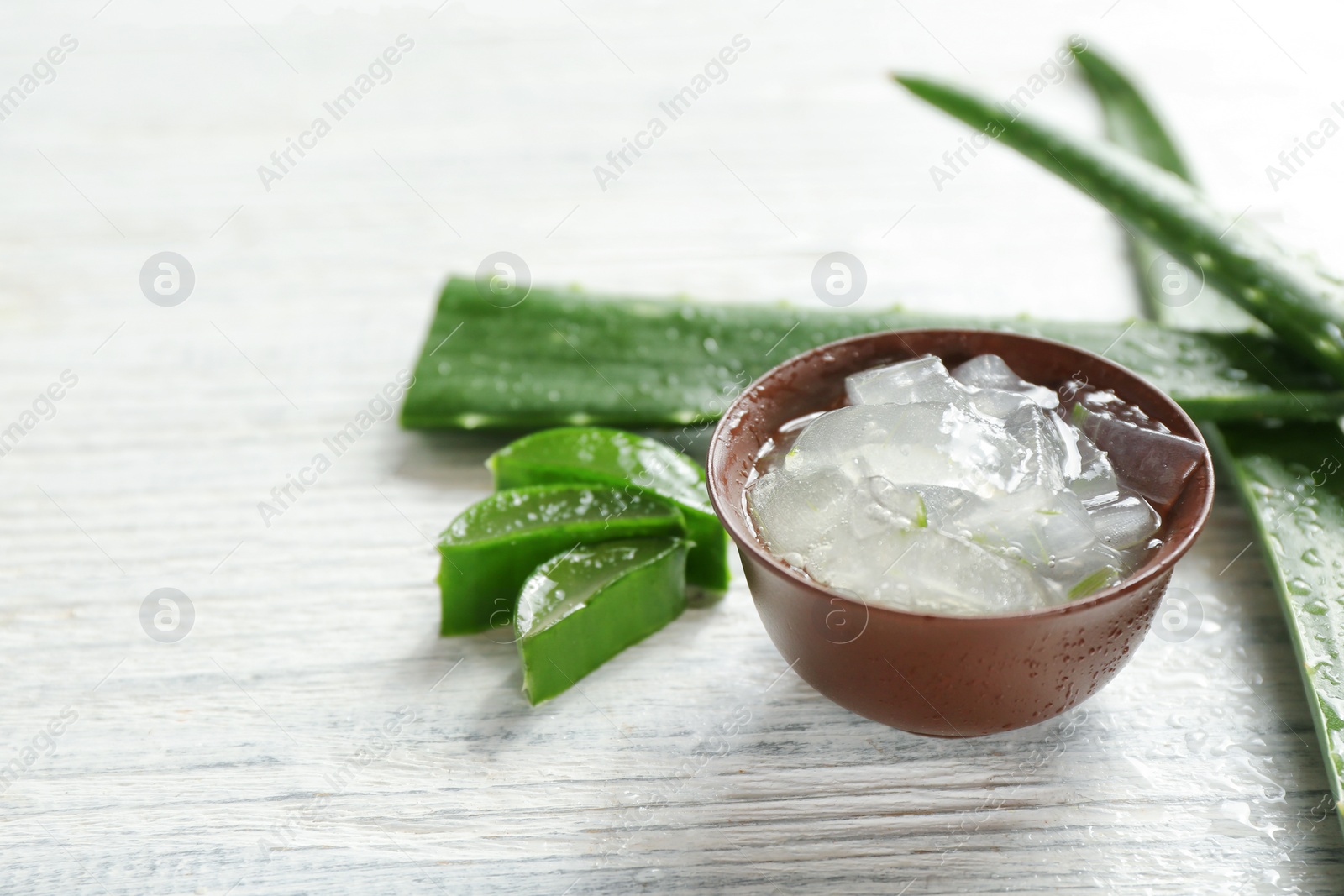 Photo of Bowl with aloe vera gel and fresh leaves on wooden table. Space for text