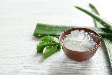 Bowl with aloe vera gel and fresh leaves on wooden table. Space for text