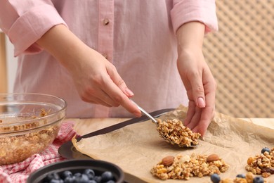 Making granola bars. Woman putting mixture of oat flakes, dry fruits and other ingredients onto baking tray at table in kitchen, closeup