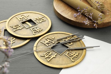 Photo of Acupuncture needles, moxa sticks and antique Chinese coins on grey wooden table, closeup