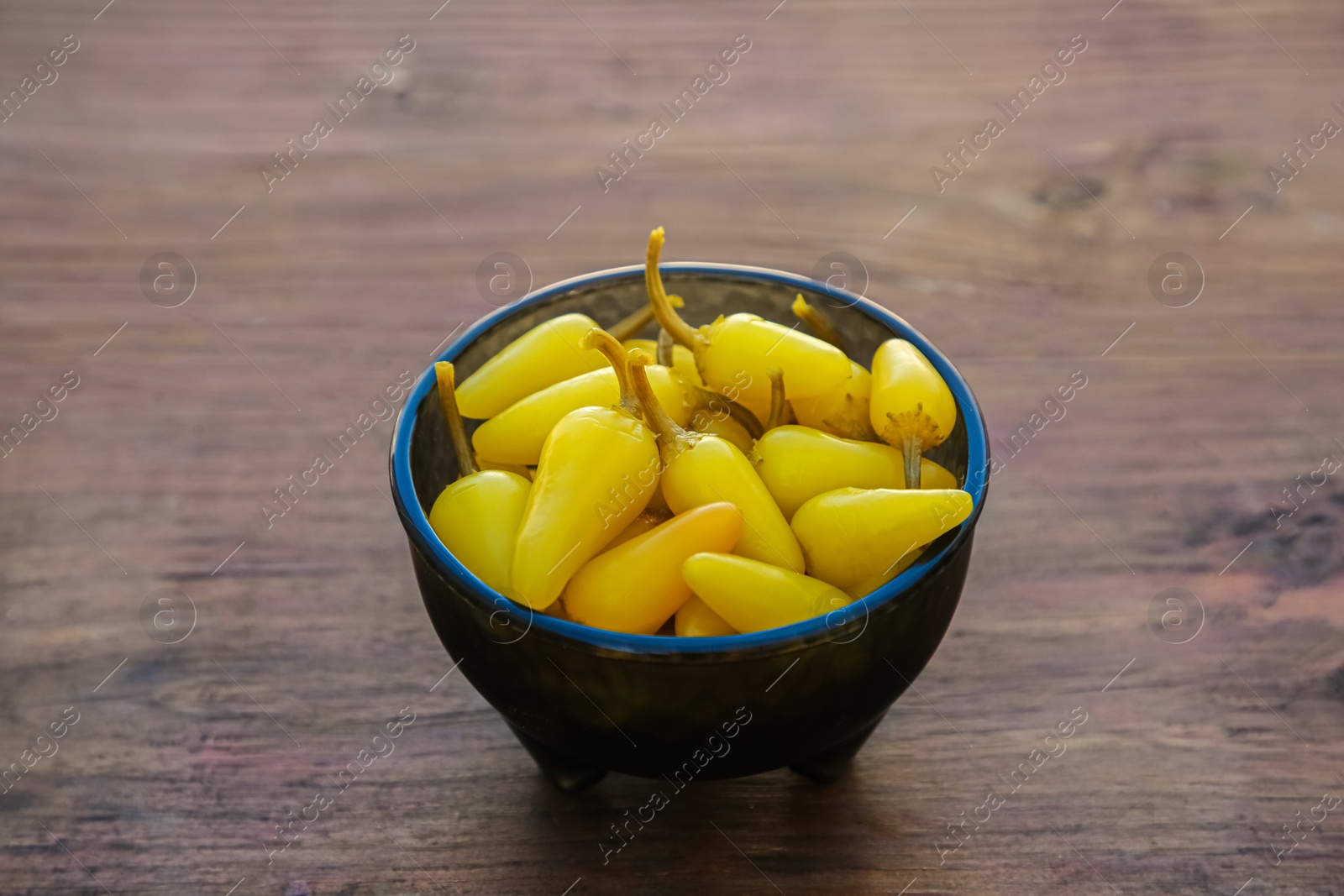 Photo of Bowl of pickled yellow jalapeno peppers on wooden table, closeup