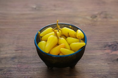 Photo of Bowl of pickled yellow jalapeno peppers on wooden table, closeup