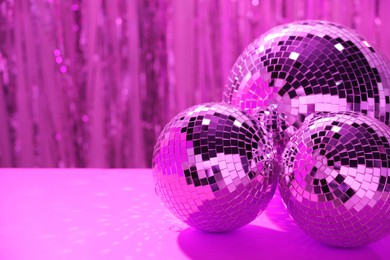 Photo of Shiny disco balls on table against blurred background, toned in pink. Space for text