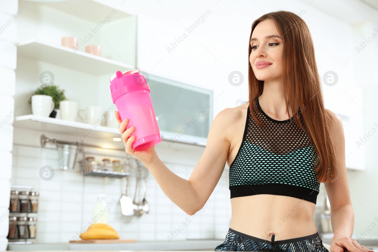 Photo of Young woman with bottle of protein shake in kitchen