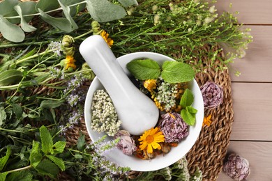 Photo of Mortar with pestle and many different herbs on wooden table, flat lay