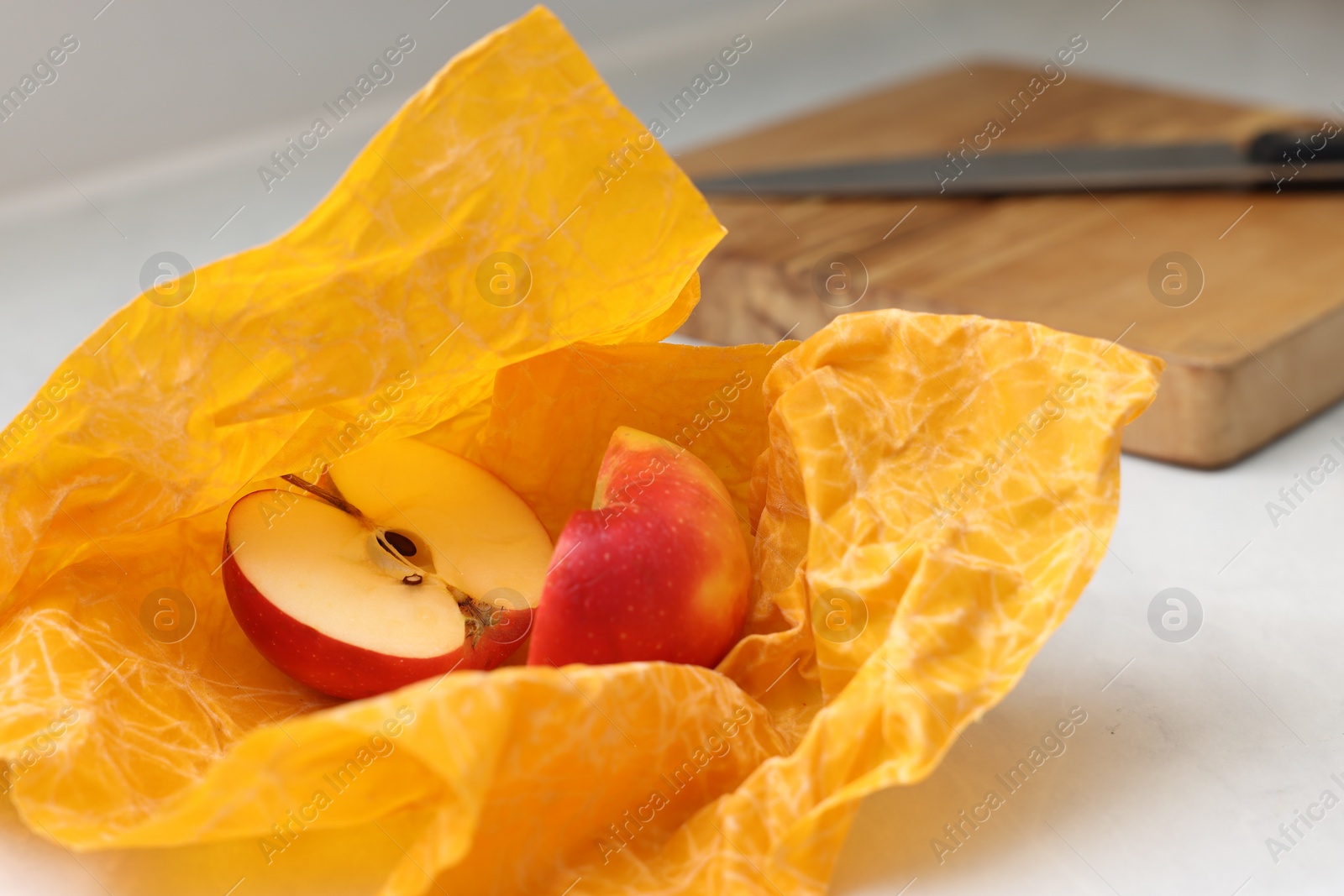 Photo of Halves of apple with orange beeswax food wrap on table, closeup