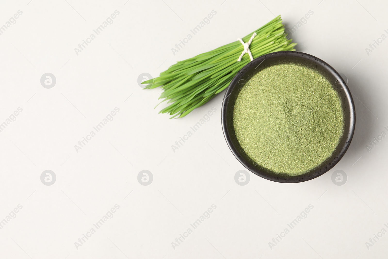 Photo of Wheat grass powder in bowl and fresh green sprouts on light table, flat lay. Space for text