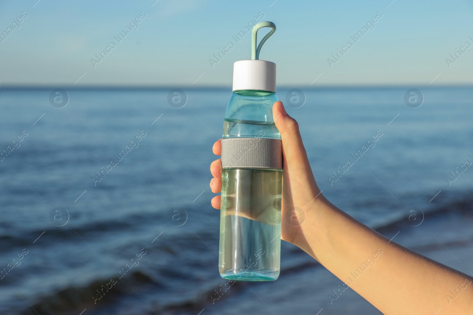 Photo of Woman holding glass bottle with water near sea, closeup