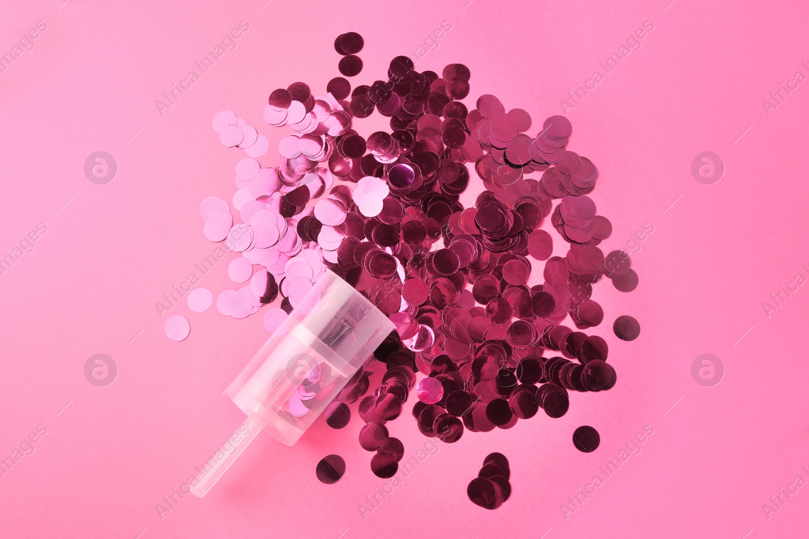 Photo of Shiny confetti bursting out of transparent party popper on pink background, flat lay