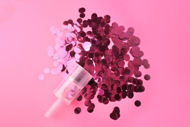 Photo of Shiny confetti bursting out of transparent party popper on pink background, flat lay