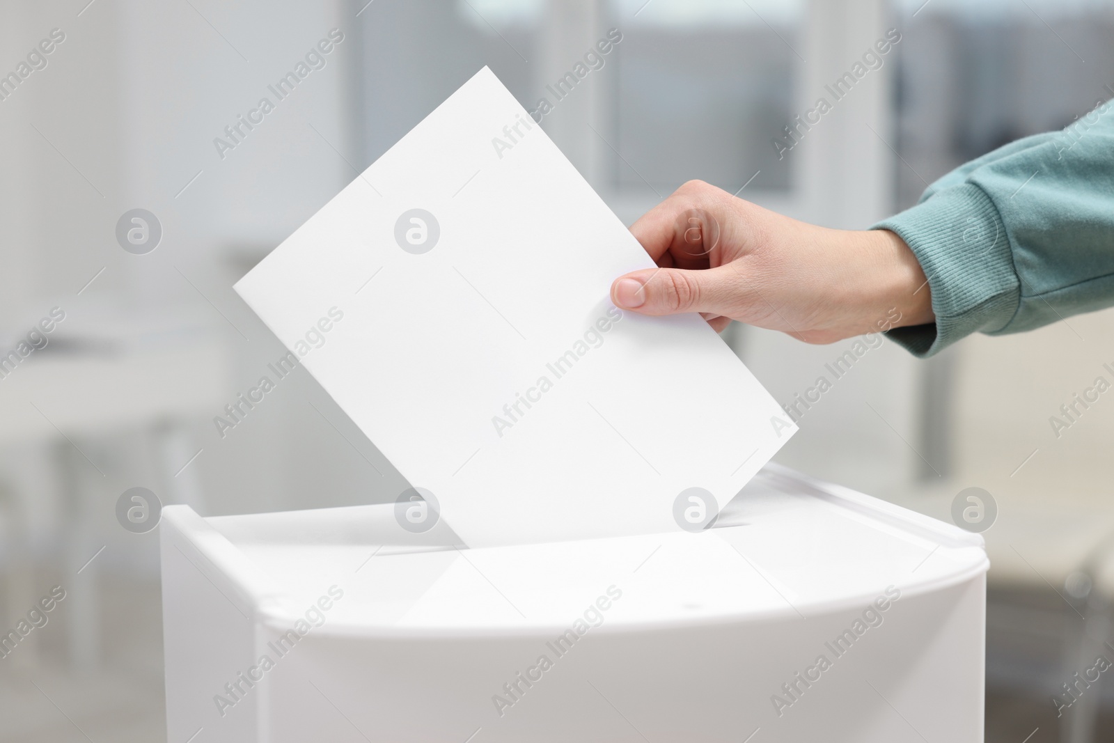 Photo of Woman putting her vote into ballot box on blurred background, closeup