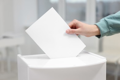 Photo of Woman putting her vote into ballot box on blurred background, closeup