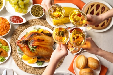 People holding glasses of wine over table with festive dinner and roasted turkey, top view