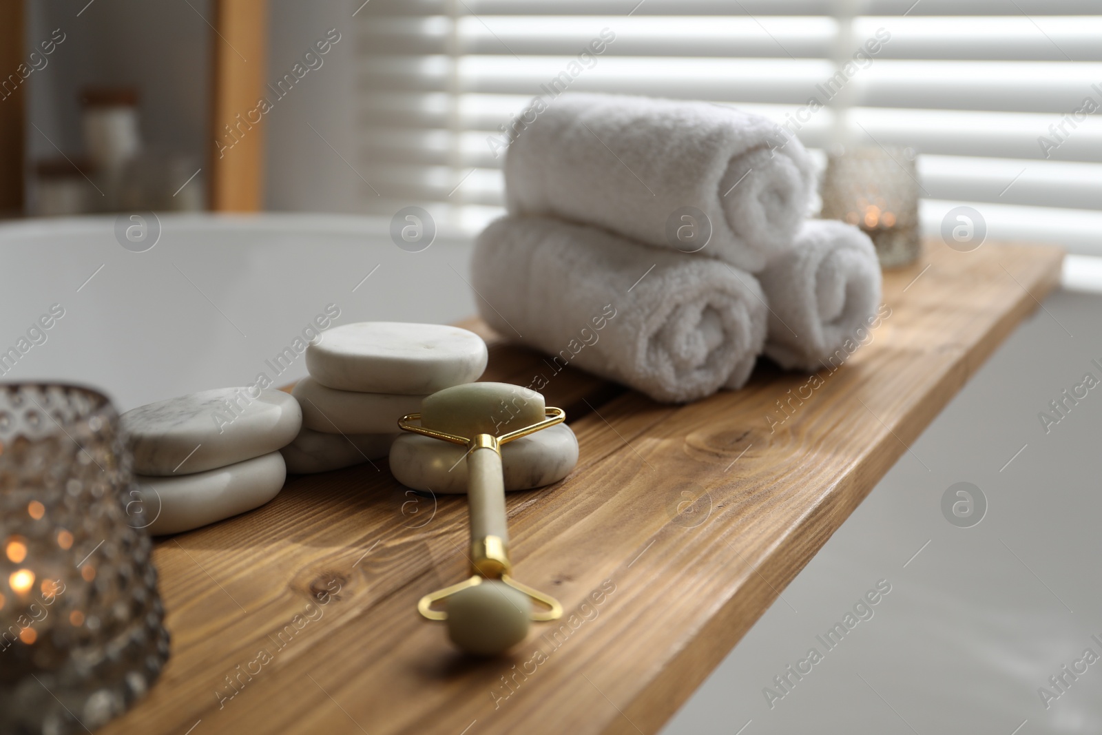 Photo of Wooden tray with spa products and candle on bath tub in bathroom, closeup