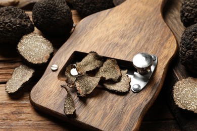 Photo of Shaver with whole and sliced black truffles on wooden table, closeup