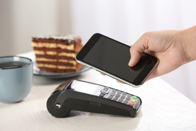 Woman using terminal for contactless payment with smartphone in cafe