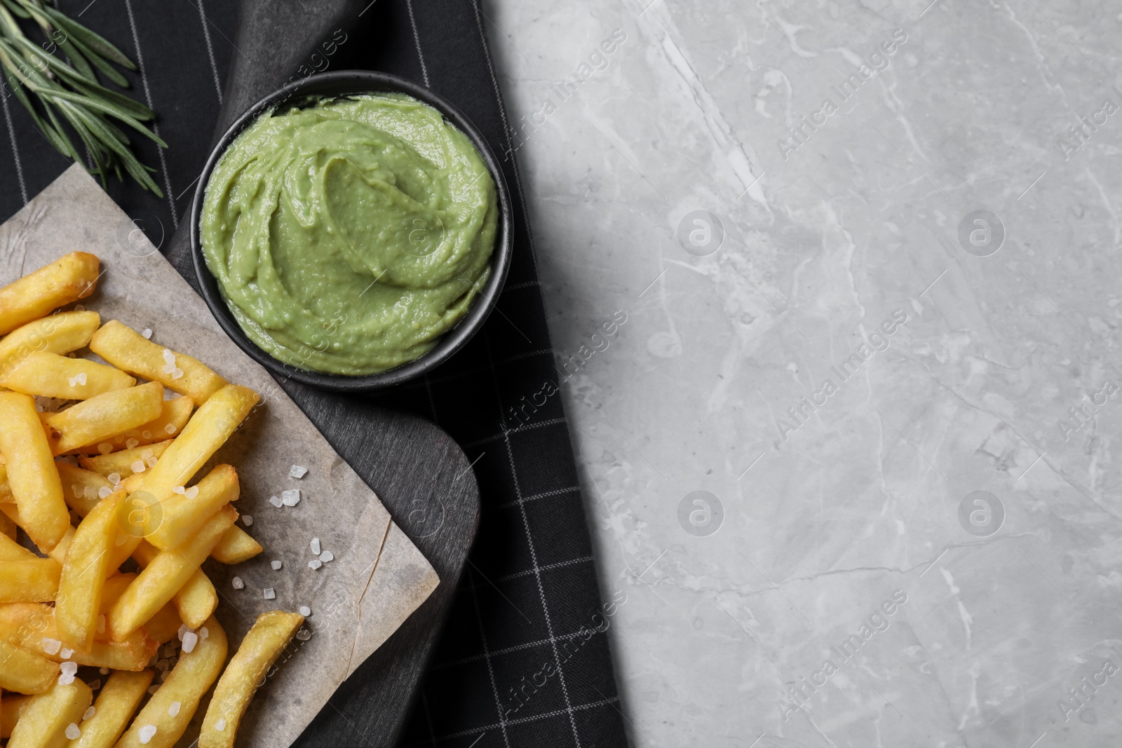 Photo of Serving board with french fries, avocado dip and rosemary on grey marble table, top view. Space for text