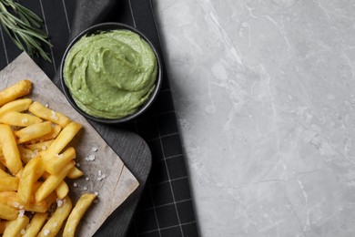 Serving board with french fries, avocado dip and rosemary on grey marble table, top view. Space for text