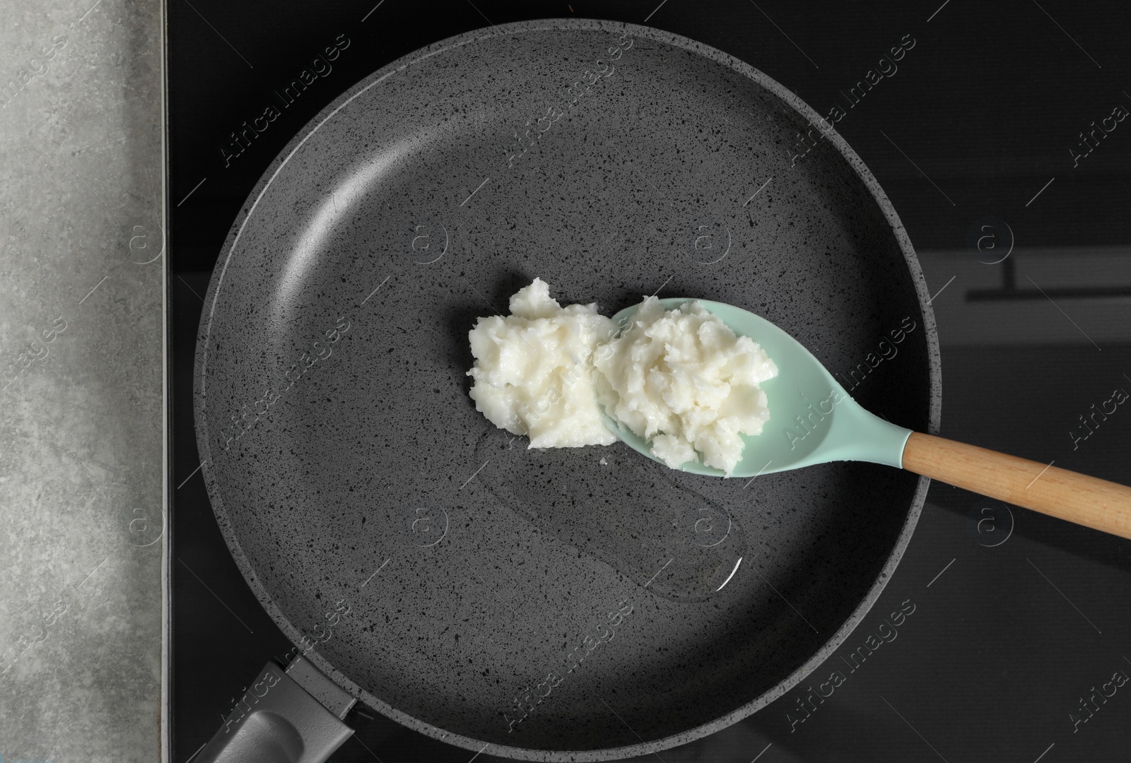 Photo of Frying pan with coconut oil and spoon on induction stove, top view. Healthy cooking