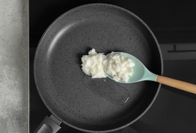 Frying pan with coconut oil and spoon on induction stove, top view. Healthy cooking