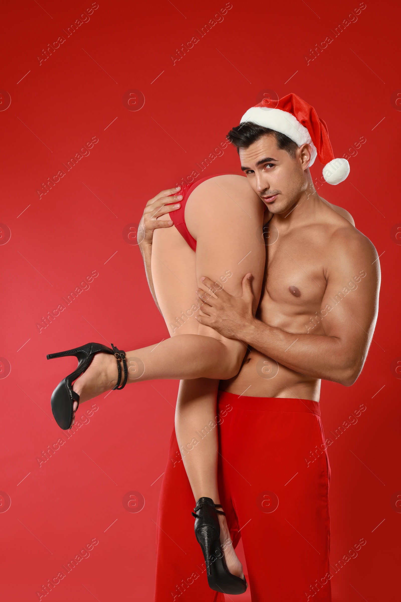 Photo of Attractive young Santa Claus with sexy woman on red background