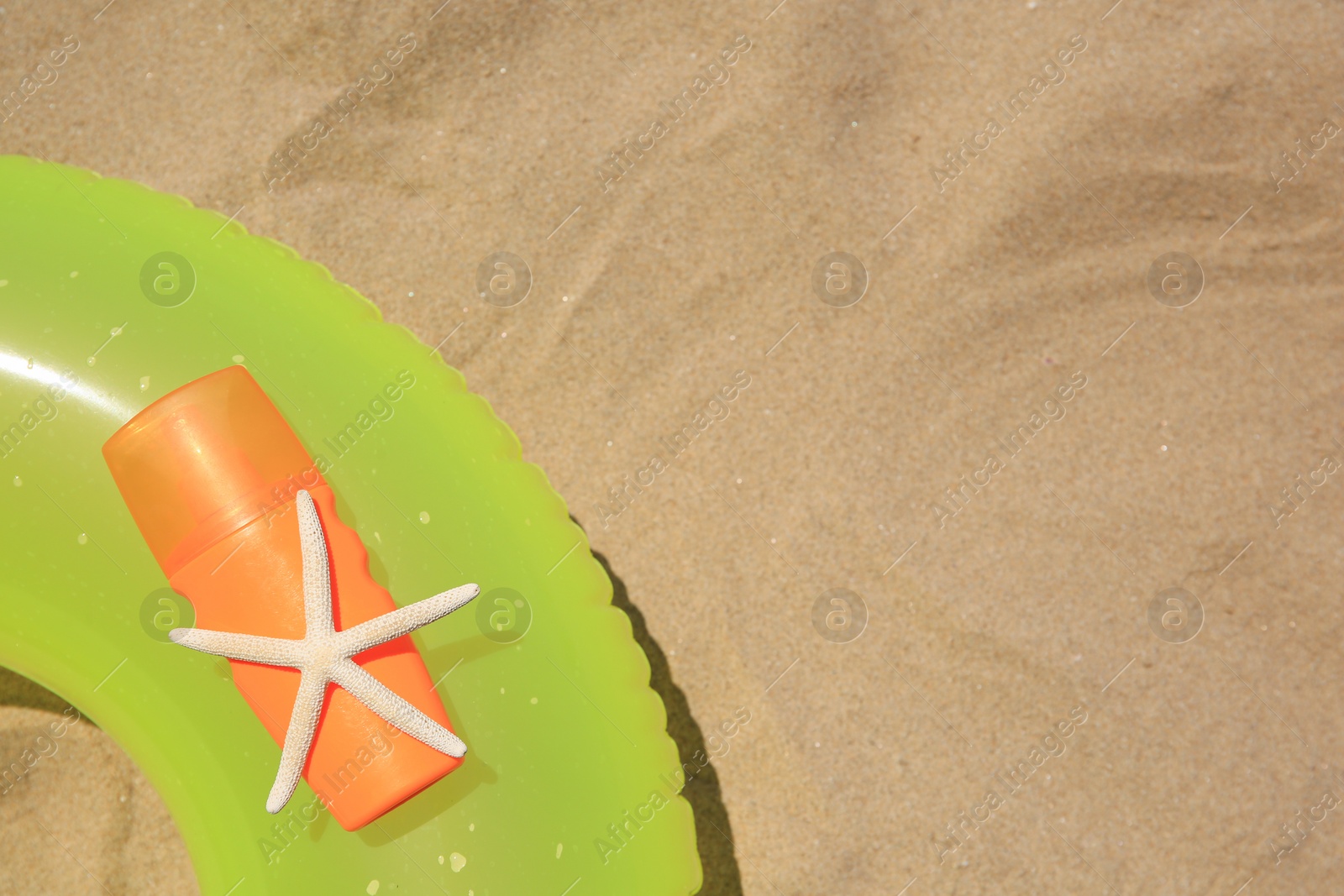 Photo of Sunscreen, starfish and inflatable ring on sand, top view with space for text. Sun protection care