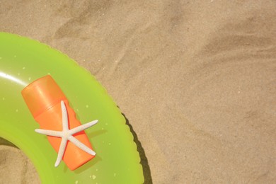 Sunscreen, starfish and inflatable ring on sand, top view with space for text. Sun protection care