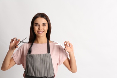 Photo of Young hairstylist holding professional scissors on light background