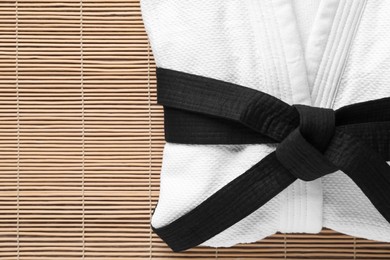 Photo of Martial arts uniform with black belt on bamboo mat, top view. Space for text