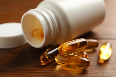 Photo of Overturned bottle with dietary supplement capsules on wooden table, closeup