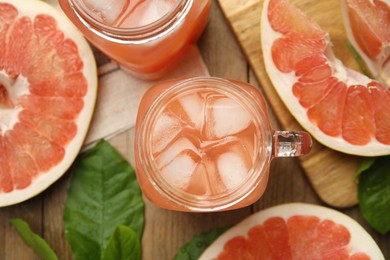 Glass jar of cold pomelo juice and fruit on wooden table, flat lay