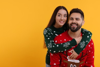 Photo of Happy young couple in Christmas sweaters on orange background. Space for text