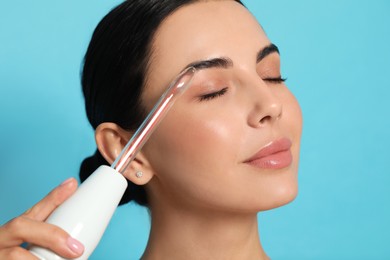 Woman using high frequency darsonval device on light blue background, closeup