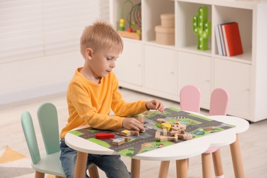 Photo of Cute little boy playing with set of wooden road signs and cars at table indoors, space for text. Child's toy
