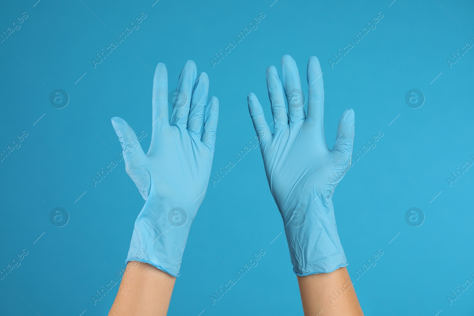 Photo of Doctor wearing medical gloves on light blue background, closeup