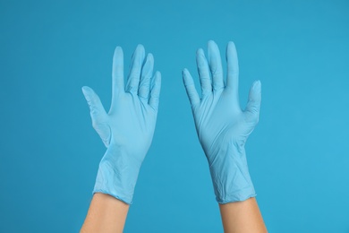 Doctor wearing medical gloves on light blue background, closeup