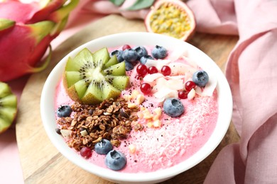 Photo of Tasty smoothie bowl with fresh kiwi fruit, berries and granola on pink table, closeup