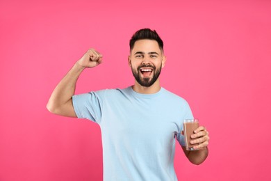 Photo of Young man with glass of chocolate milk showing his strength on pink background