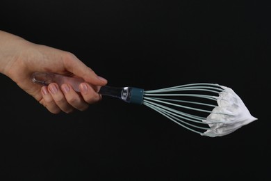 Photo of Woman holding whisk with whipped cream on black background, closeup