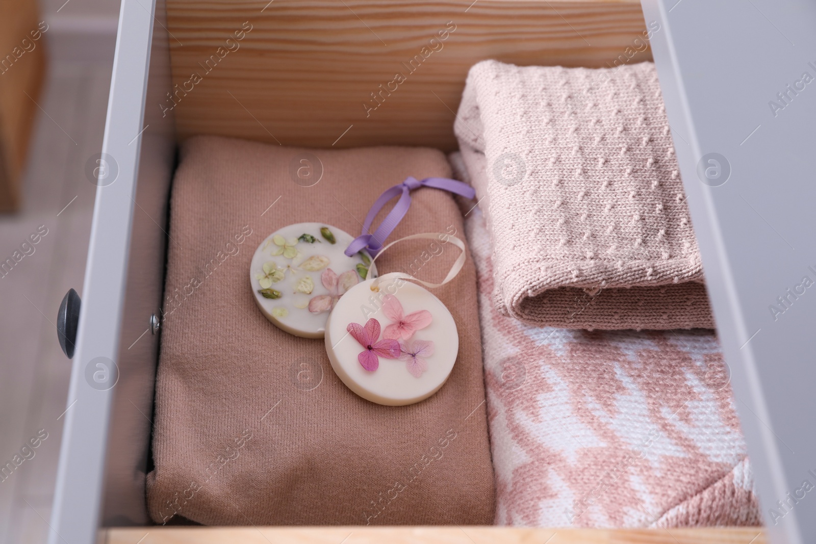 Photo of Beautiful scented wax sachets and clothes in dresser drawer, closeup