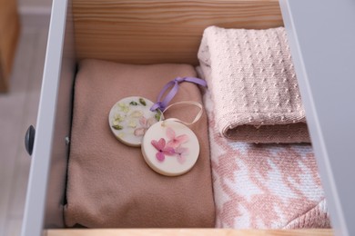 Photo of Beautiful scented wax sachets and clothes in dresser drawer, closeup