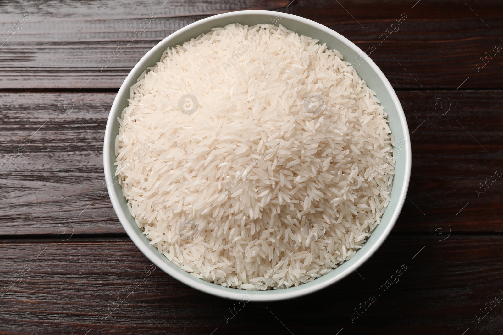 Photo of Raw basmati rice in bowl on wooden table, top view