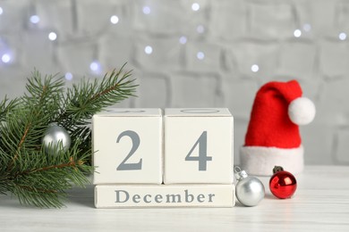 Photo of December 24 - Christmas Eve. Wooden block calendar and decor on white table against blurred festive lights