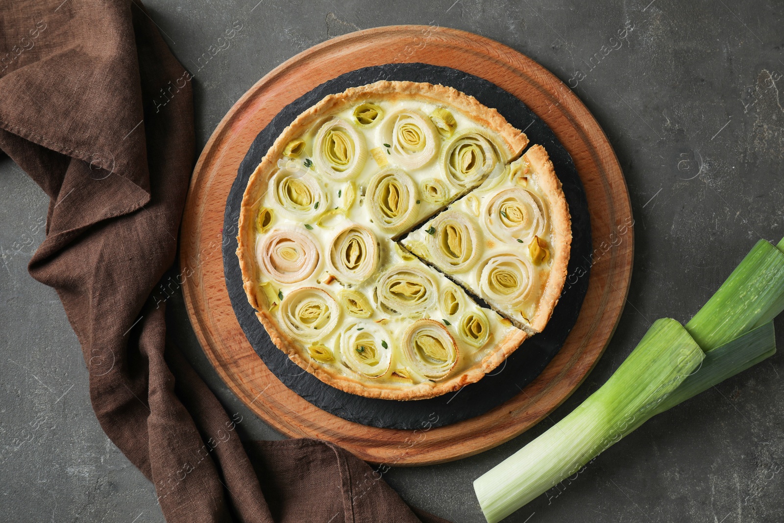 Photo of Tasty leek pie and fresh stalk on dark textured table, flat lay