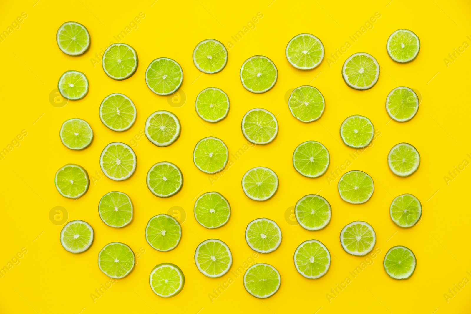 Photo of Slices of fresh juicy limes on yellow background, flat lay