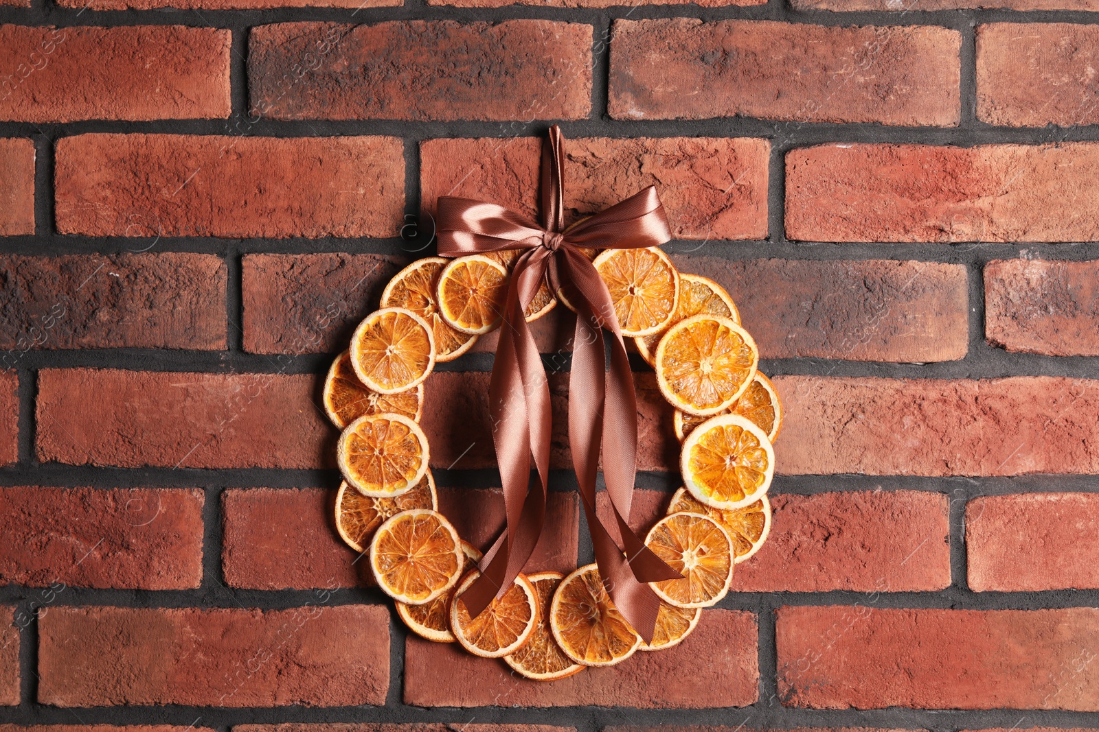 Photo of Decorative wreath made with dry oranges and ribbon hanging on red brick wall