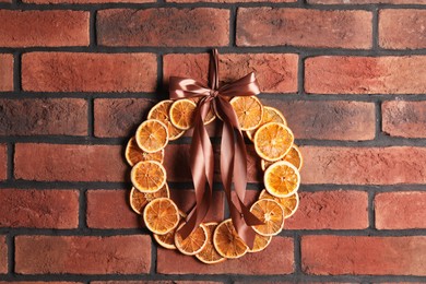 Photo of Decorative wreath made with dry oranges and ribbon hanging on red brick wall