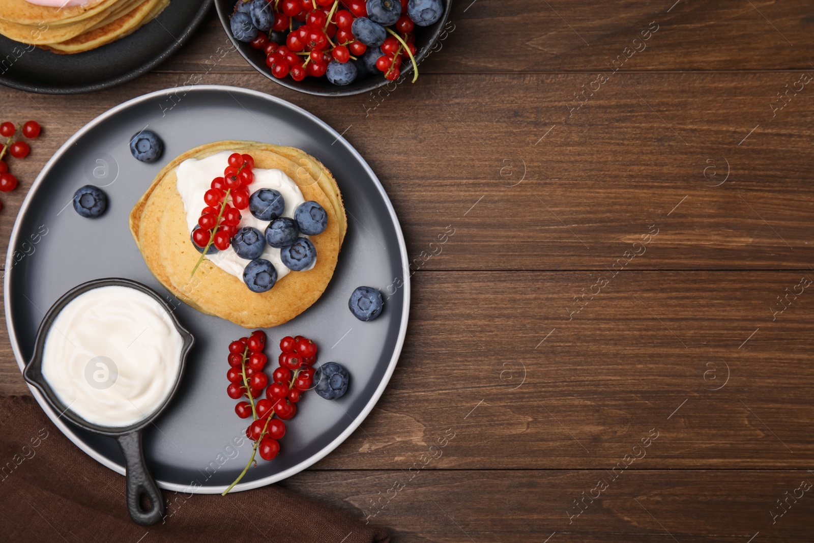 Photo of Tasty pancakes with natural yogurt, blueberries and red currants on wooden table, flat lay. Space for text