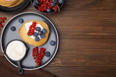 Photo of Tasty pancakes with natural yogurt, blueberries and red currants on wooden table, flat lay. Space for text