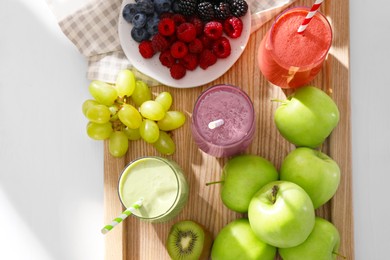 Photo of Glasses of different tasty smoothies and fresh ingredients on white wooden table, top view